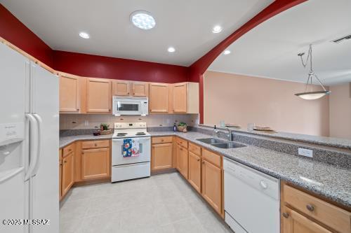 kitchen with light stone counters, white appliances, sink, and light brown cabinets