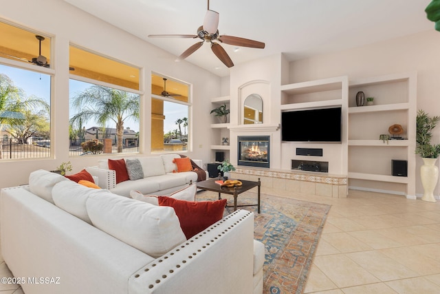 living area with a tiled fireplace, tile patterned floors, built in features, and a ceiling fan