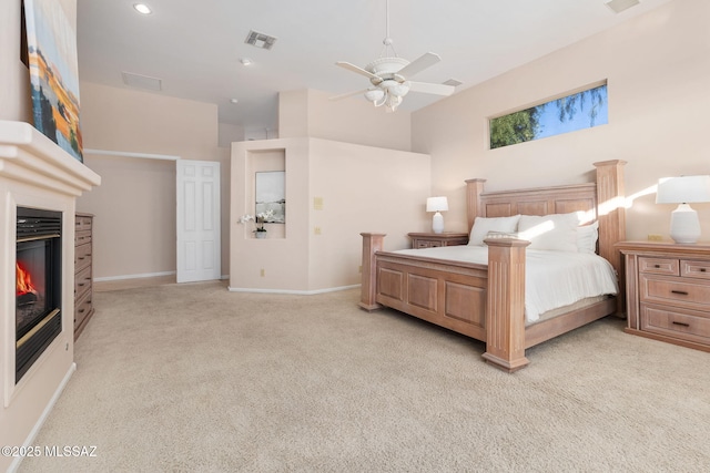 bedroom with visible vents, a ceiling fan, a glass covered fireplace, baseboards, and light colored carpet