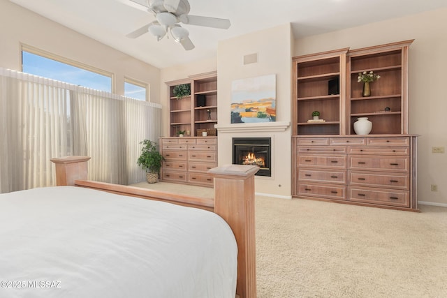 carpeted bedroom featuring a glass covered fireplace, baseboards, visible vents, and ceiling fan