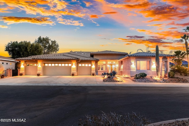 view of front of home with stucco siding, driveway, a tile roof, and an attached garage