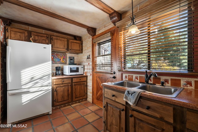 kitchen with brown cabinetry, beamed ceiling, light tile patterned flooring, hanging light fixtures, and white appliances