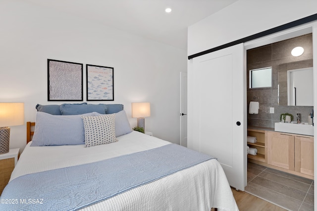 bedroom with sink, ensuite bath, light hardwood / wood-style flooring, and a barn door