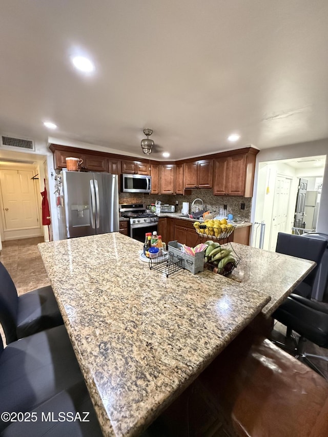 kitchen with sink, backsplash, a kitchen bar, light stone counters, and stainless steel appliances