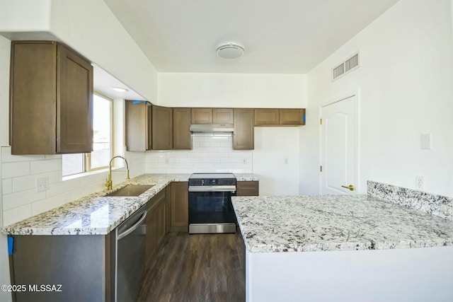 kitchen featuring sink, decorative backsplash, light stone counters, stainless steel appliances, and dark wood-type flooring