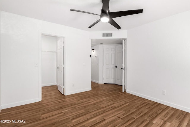 unfurnished bedroom featuring a walk in closet, dark hardwood / wood-style floors, ceiling fan, and a closet