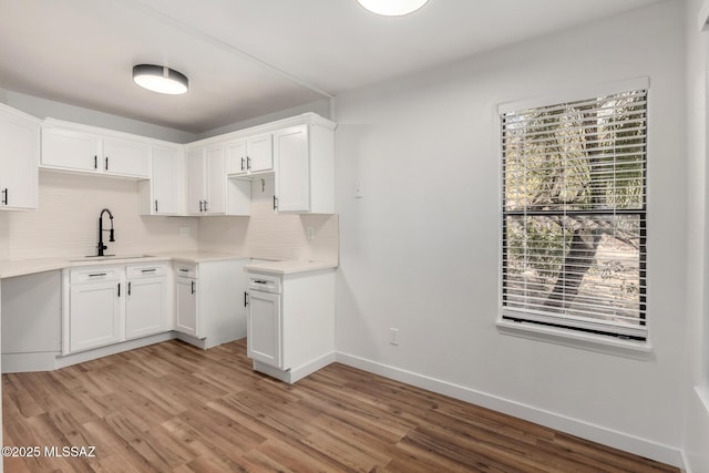 kitchen with tasteful backsplash, sink, white cabinets, and light wood-type flooring