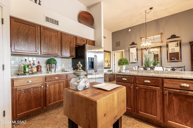 kitchen with stainless steel fridge, backsplash, hanging light fixtures, light tile patterned floors, and light stone countertops