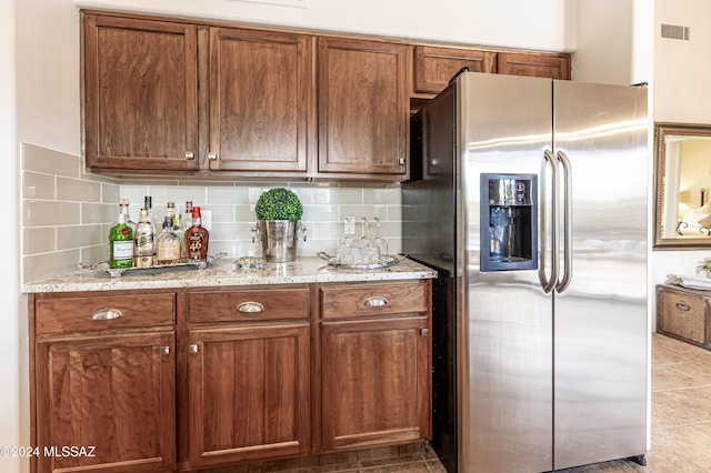 kitchen with tasteful backsplash, light tile patterned flooring, light stone counters, and stainless steel fridge with ice dispenser