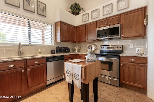 kitchen with stainless steel appliances, tasteful backsplash, light stone countertops, and sink