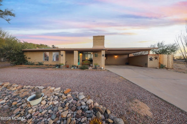 view of front of house with an attached carport, concrete driveway, brick siding, and a chimney