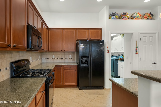 kitchen featuring light tile patterned floors, light stone countertops, black appliances, washing machine and clothes dryer, and decorative backsplash