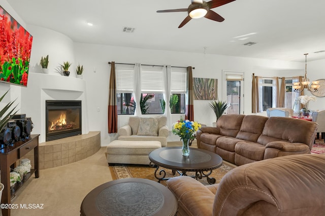 carpeted living room featuring a tiled fireplace and ceiling fan with notable chandelier