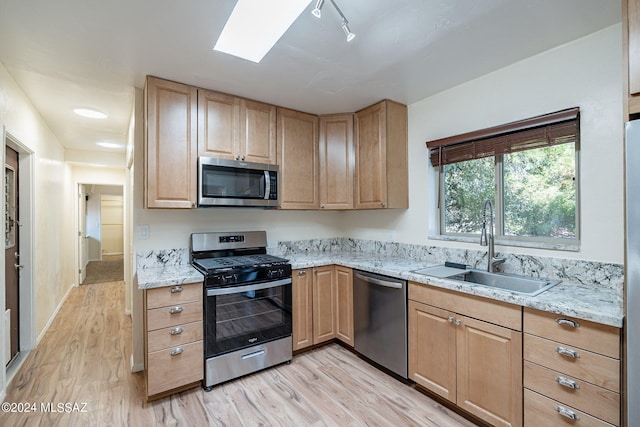 kitchen with light brown cabinetry, sink, light stone counters, light wood-type flooring, and stainless steel appliances