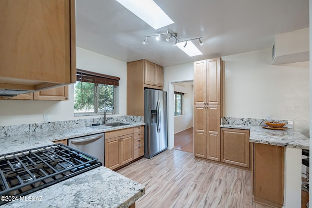 kitchen featuring a skylight, sink, light stone counters, stainless steel appliances, and light wood-type flooring