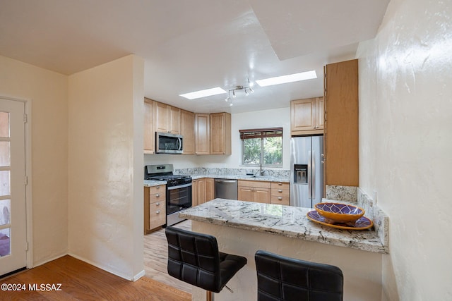 kitchen with a kitchen bar, light stone counters, kitchen peninsula, stainless steel appliances, and light hardwood / wood-style floors