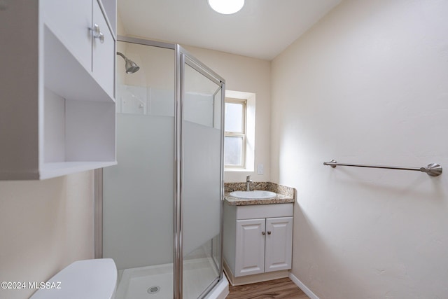 bathroom with hardwood / wood-style flooring, vanity, a shower with shower door, and toilet