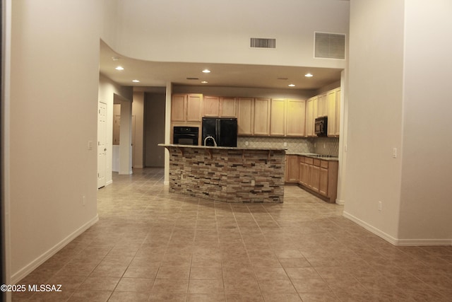 kitchen with light brown cabinetry, backsplash, black appliances, and a center island with sink