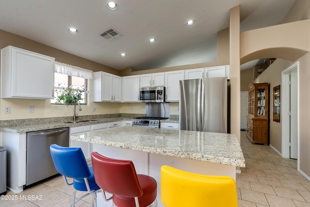 kitchen with sink, stainless steel appliances, a center island, light stone counters, and white cabinets