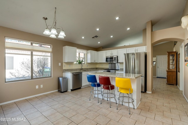 kitchen with light stone counters, hanging light fixtures, a kitchen island, stainless steel appliances, and white cabinets