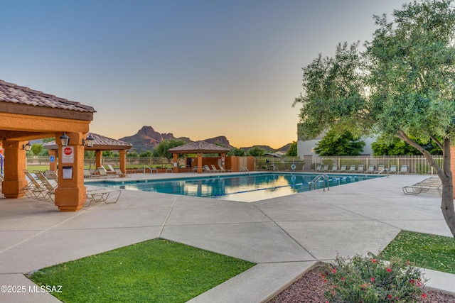 pool at dusk with a gazebo and a patio area