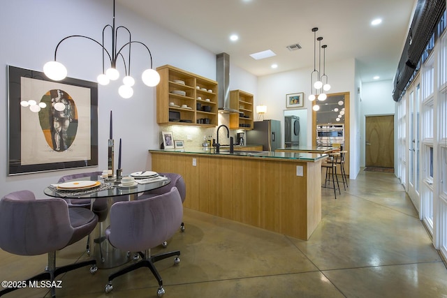 kitchen with appliances with stainless steel finishes, pendant lighting, sink, decorative backsplash, and wall chimney range hood