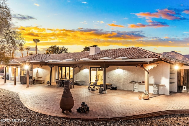 back house at dusk with exterior kitchen and a patio area