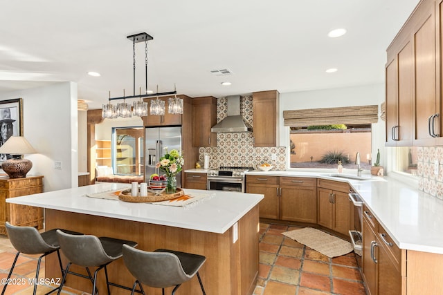 kitchen featuring wall chimney exhaust hood, sink, a center island, appliances with stainless steel finishes, and decorative backsplash