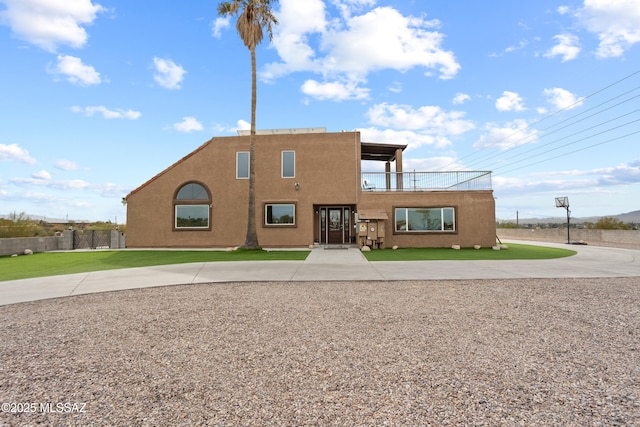 view of front of property with a front lawn, fence, a balcony, and stucco siding