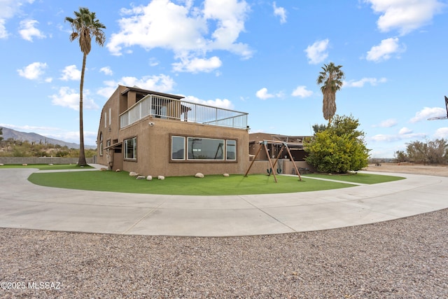 view of front facade featuring concrete driveway, a balcony, a mountain view, a front lawn, and stucco siding