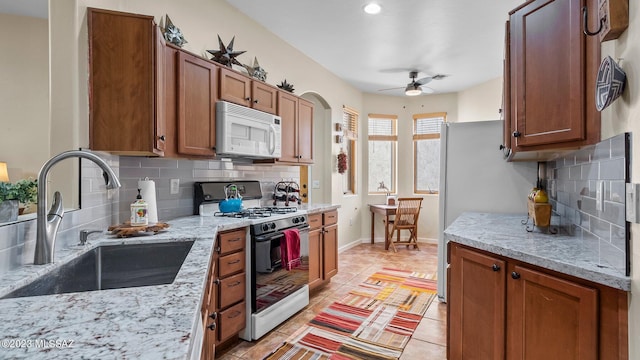 kitchen featuring sink, tasteful backsplash, range with gas stovetop, ceiling fan, and light stone countertops