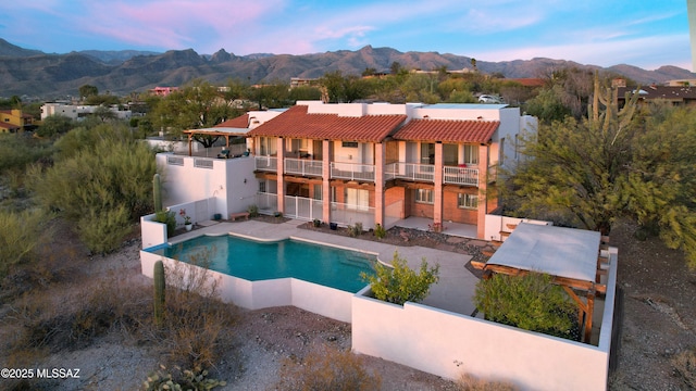 back of house featuring a balcony, a mountain view, fence, a tiled roof, and a patio area