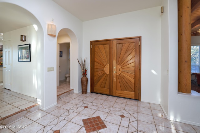 entryway featuring arched walkways, light tile patterned flooring, and baseboards