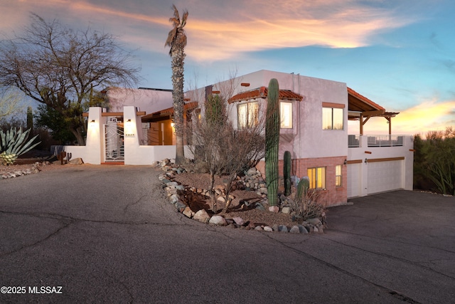 pueblo-style home featuring an attached garage, a balcony, driveway, a gate, and stucco siding