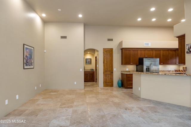 kitchen with light stone counters, stainless steel fridge with ice dispenser, and a high ceiling