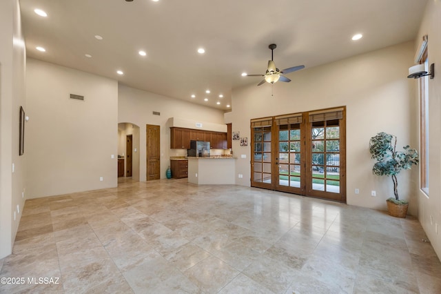 unfurnished living room with a towering ceiling, french doors, and ceiling fan