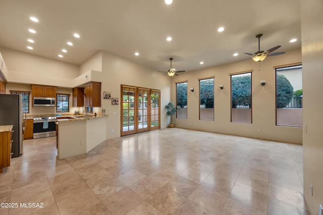 kitchen with french doors, kitchen peninsula, ceiling fan, stainless steel appliances, and light stone countertops