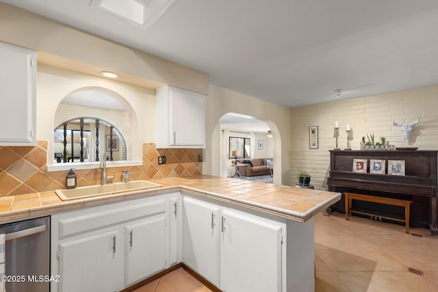 kitchen with tile countertops, sink, white cabinets, stainless steel dishwasher, and kitchen peninsula