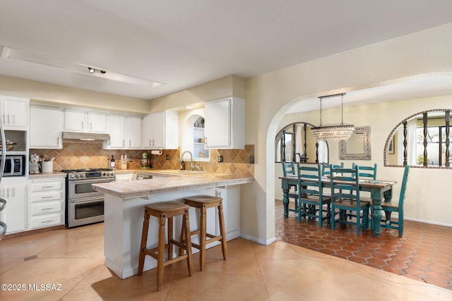 kitchen featuring sink, appliances with stainless steel finishes, kitchen peninsula, pendant lighting, and white cabinets