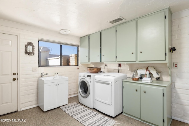 laundry area with cabinets, brick wall, washer and clothes dryer, and sink