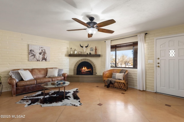 living room featuring ceiling fan, brick wall, tile patterned floors, and a fireplace