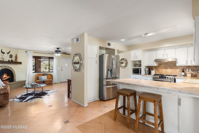 kitchen featuring a breakfast bar, tile countertops, stainless steel appliances, decorative backsplash, and white cabinets