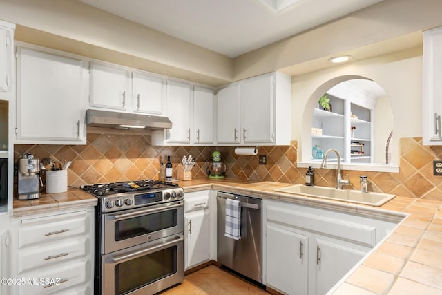 kitchen with sink, appliances with stainless steel finishes, tasteful backsplash, tile counters, and white cabinets