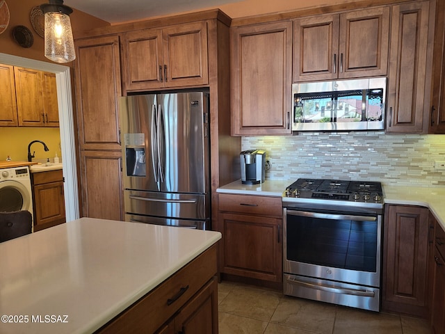 kitchen with sink, appliances with stainless steel finishes, washer / clothes dryer, decorative backsplash, and decorative light fixtures