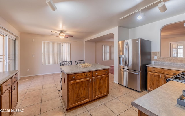 8497 E Hodgman Pl, Tucson, AZ 85747 - kitchen with stainless steel refrigerator with ice dispenser, arched walkways, ceiling fan, light tile patterned floors, and brown cabinets