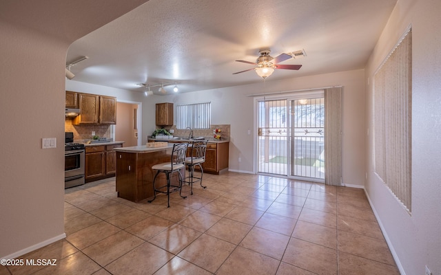 8497 E Hodgman Pl, Tucson, AZ 85747 - kitchen featuring stainless steel gas range oven, decorative backsplash, under cabinet range hood, a breakfast bar area, and brown cabinets