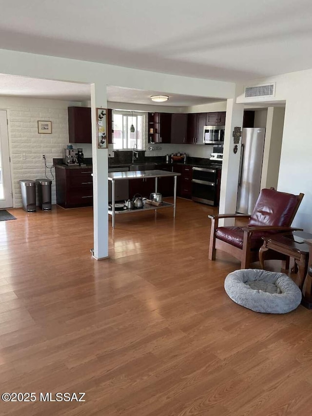 kitchen featuring dark brown cabinetry, appliances with stainless steel finishes, brick wall, and wood-type flooring