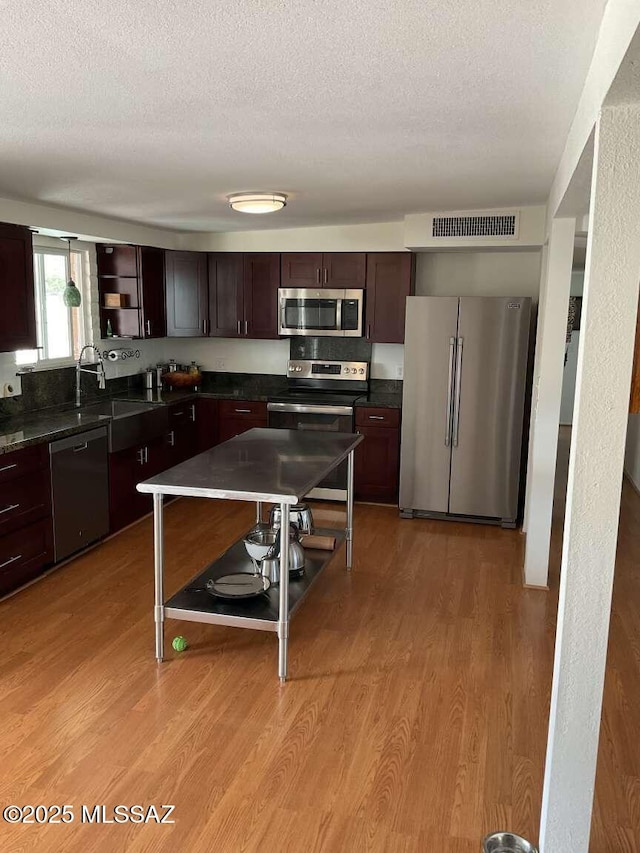 kitchen with appliances with stainless steel finishes, sink, dark brown cabinetry, and light hardwood / wood-style flooring