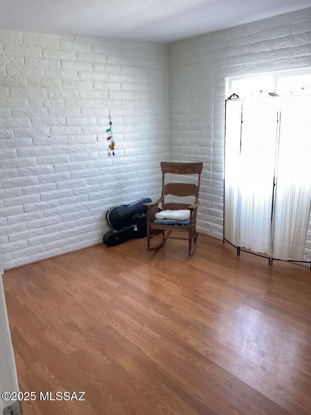 unfurnished room featuring hardwood / wood-style flooring and brick wall