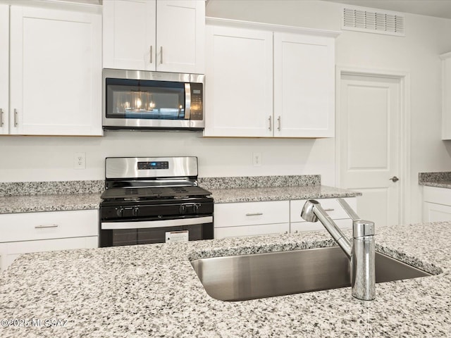 kitchen featuring visible vents, light stone counters, appliances with stainless steel finishes, white cabinetry, and a sink